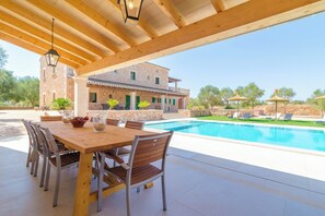 Une terrasse en bois avec une piscine, des sièges d’extérieur et un bâtiment en pierre en arrière-plan.