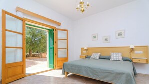Une chambre à coucher avec un lit, une table de chevet, une lampe et une vue sur l’extérieur, visible à travers une porte ouverte.