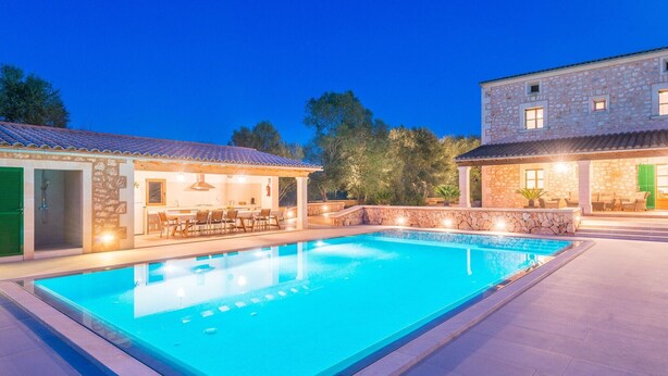Une piscine avec un bâtiment en pierre et un espace patio couvert.