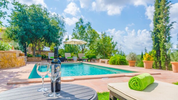 A poolside setting with a table, a bottle, and a rolled towel. - Es Garroveral 3  - Villa With Private Pool (Bunyola, Illes Balears)