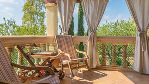 A covered outdoor seating area with two striped chairs, a small table, and a wooden cart. - Es Garroveral 3  - Villa With Private Pool (Bunyola, Illes Balears)