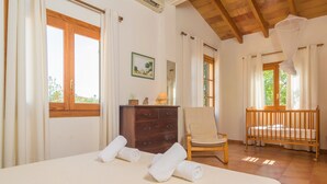 A bedroom with a bed, a wooden dresser, a chair, a crib, and a window with curtains. - Es Garroveral 3  - Villa With Private Pool (Bunyola, Illes Balears)
