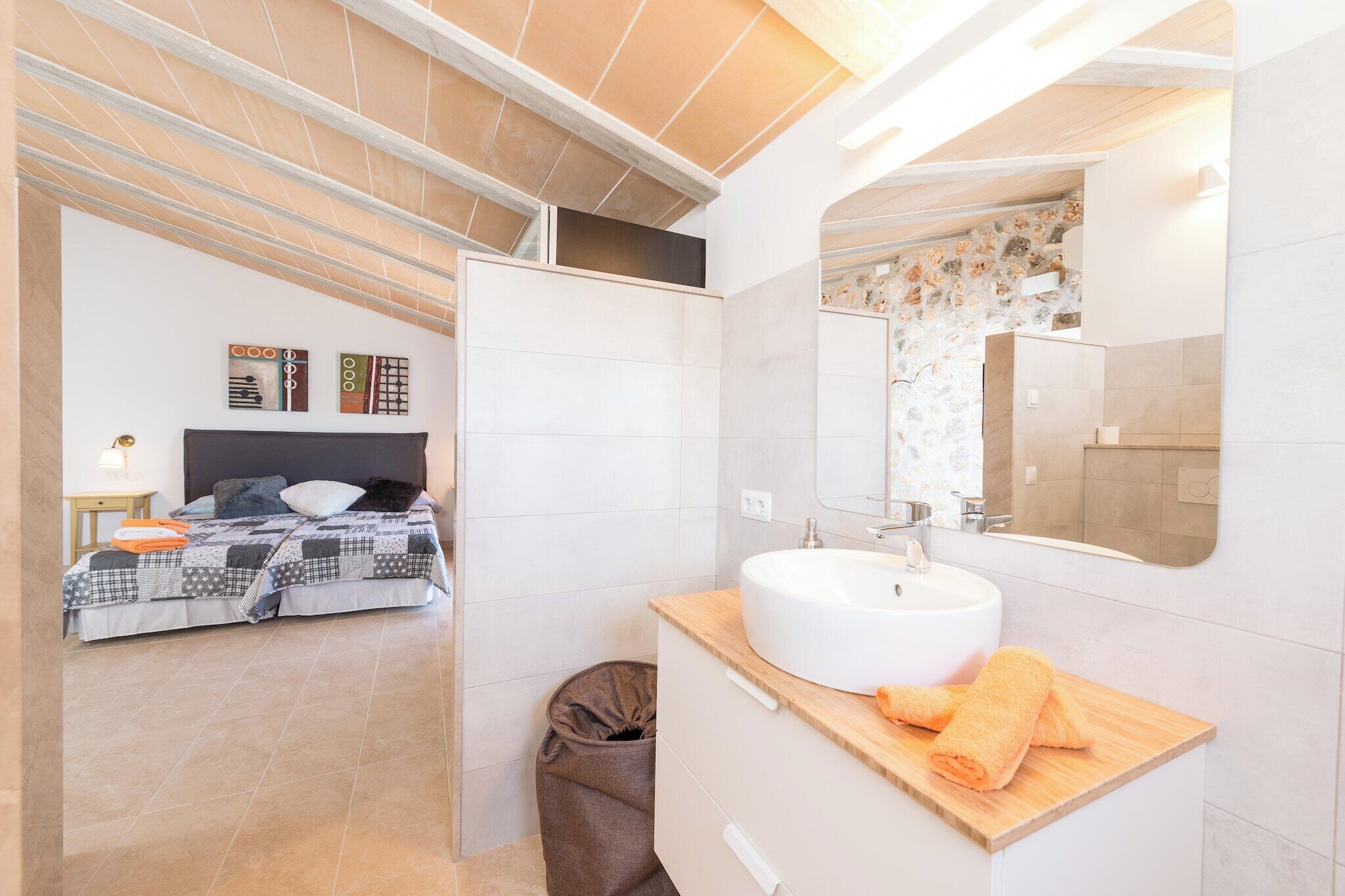 Un dormitorio moderno con cama, mesita de noche y baño con lavamanos y espejo.