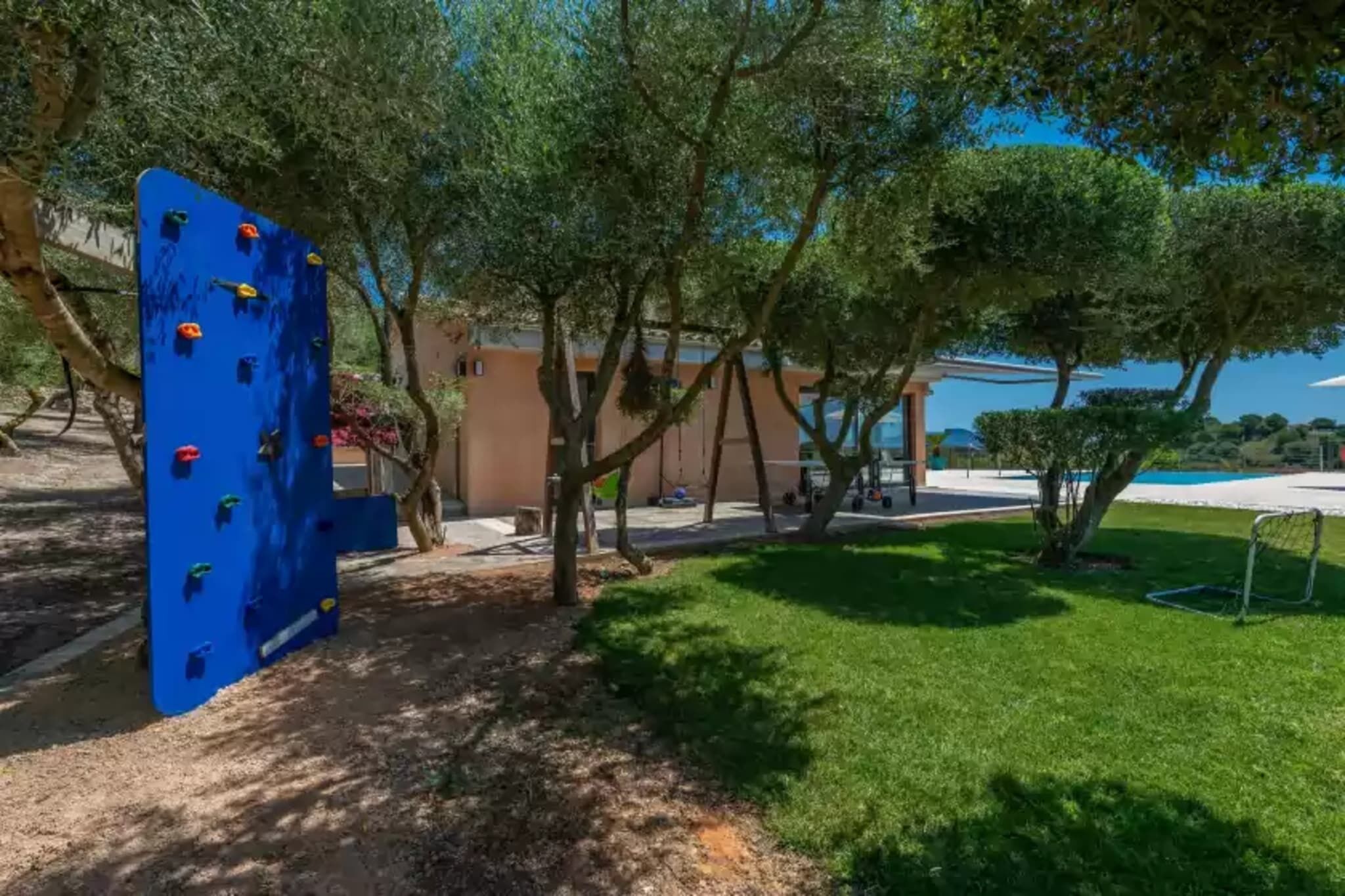 Un mur d’escalade, des arbres et une zone herbeuse, avec un bâtiment en arrière-plan.