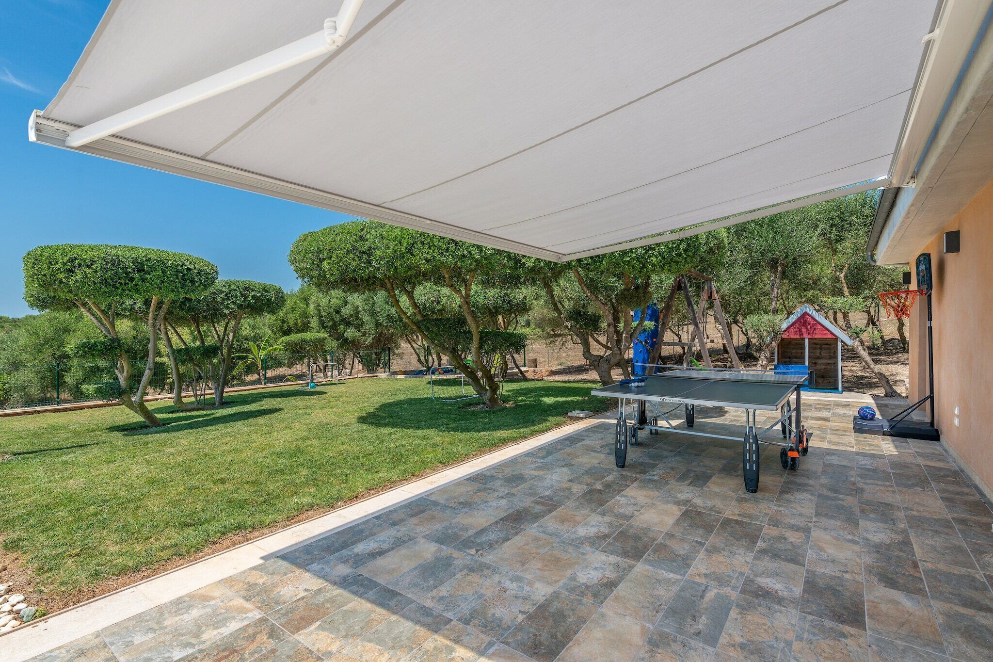 Un espace extérieur aménagé en patio, avec une table et des chaises, entouré d’une pelouse et d’arbres.