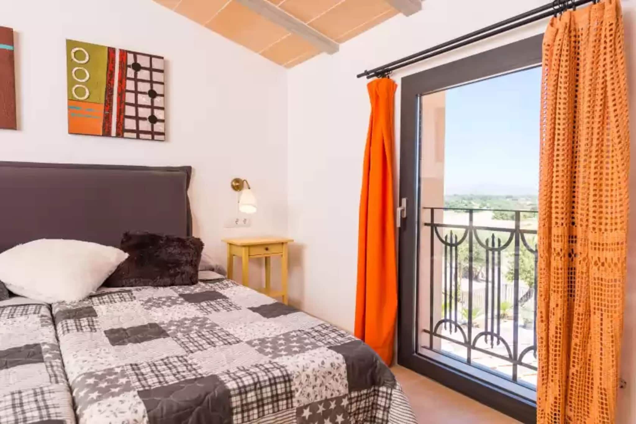 A bedroom with a bed, a nightstand, a wall clock, and a balcony with orange curtains.