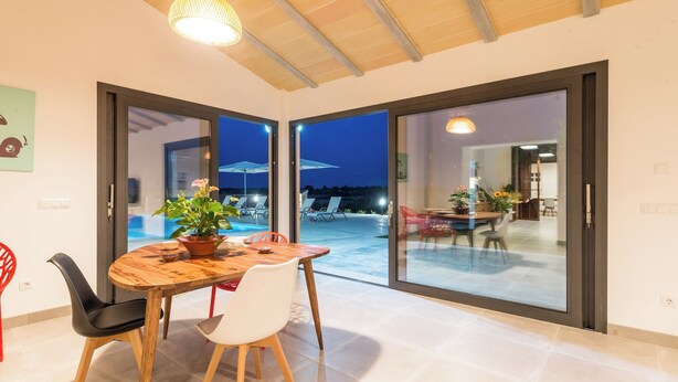 A dining area with a wooden table and chairs, large sliding glass doors leading to an outdoor patio with chairs and umbrellas. - Son Vador - Villa With Private Pool. Free Wifi (Santa Margalida, Illes Balears)