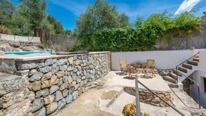 Un patio con paredes de piedra, una piscina, mobiliario exterior y una escalera que lleva a un nivel superior.