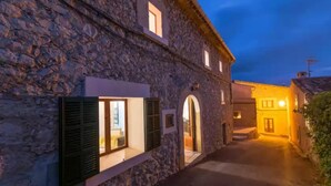 Un edificio de piedra con un estrecho callejón, puertas en arco y ventanas con contraventanas.