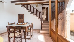 Un comedor con mesa y sillas de madera, una escalera con barandilla de madera y vistas a través de un ventanal.