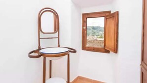 Un baño con una silla de madera, un inodoro y una ventana con vistas al paisaje.
