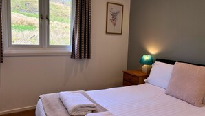 A neatly made bed with a folded towel, a bedside lamp, and a framed artwork on the wall. - Skye -  a chalet that sleeps 3 guests  in 2 bedrooms (Oban)