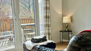 A living room with a leather sofa, a small table with a lamp, and a view through large glass doors to an outdoor deck.