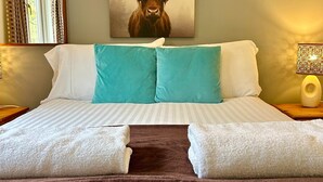 A hotel room with a bed, two pillows, a blanket, a wall-mounted artwork of a bull, a window with curtains, and a bedside lamp.