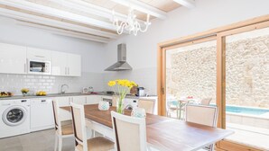 A modern kitchen with white cabinets, a wooden dining table, and a stone wall. - Can Diana - Villa With Private Pool In Campanet (Campanet, Illes Balears)