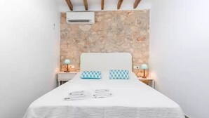 A bedroom with a stone wall, a white bed, two bedside lamps, and a ceiling fan. - Can Diana - Villa With Private Pool In Campanet (Campanet, Illes Balears)