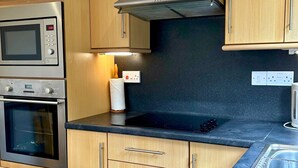 Una cocina con microondas, horno y estufa. Se observa un rodillo de toallas de papel y un enchufe en la pared.