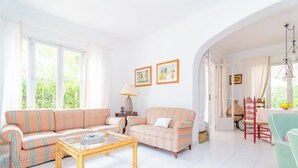 A bright living room with striped sofas, a glass coffee table, and a dining area with a table and chairs. - Can Ferro - Villa With Private Pool In Cala Blava (Cala Blava (llucmajor), Illes Balears)