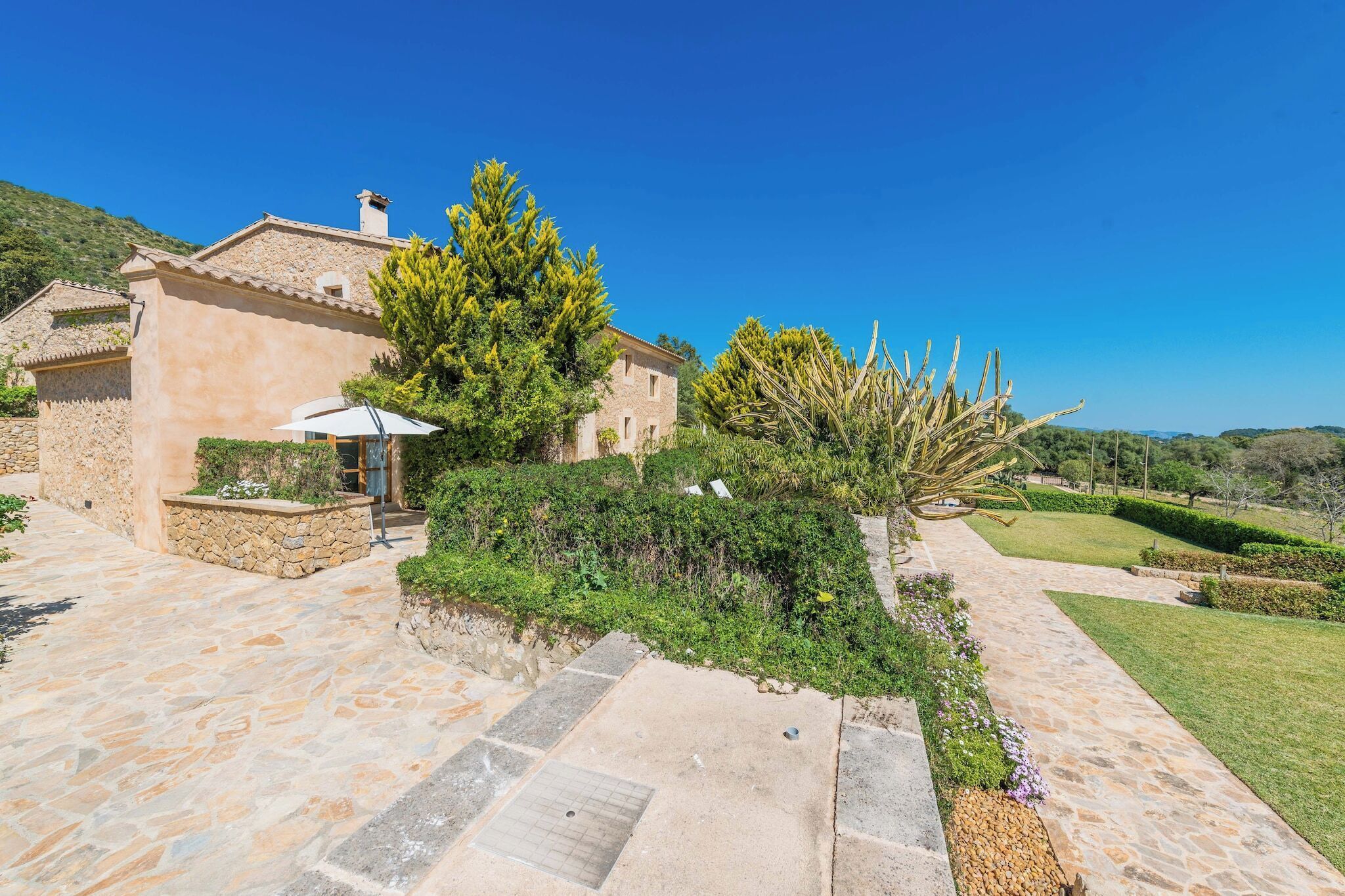 A stone building with a tiled roof, surrounded by a well-maintained garden with various plants and a clear pathway.