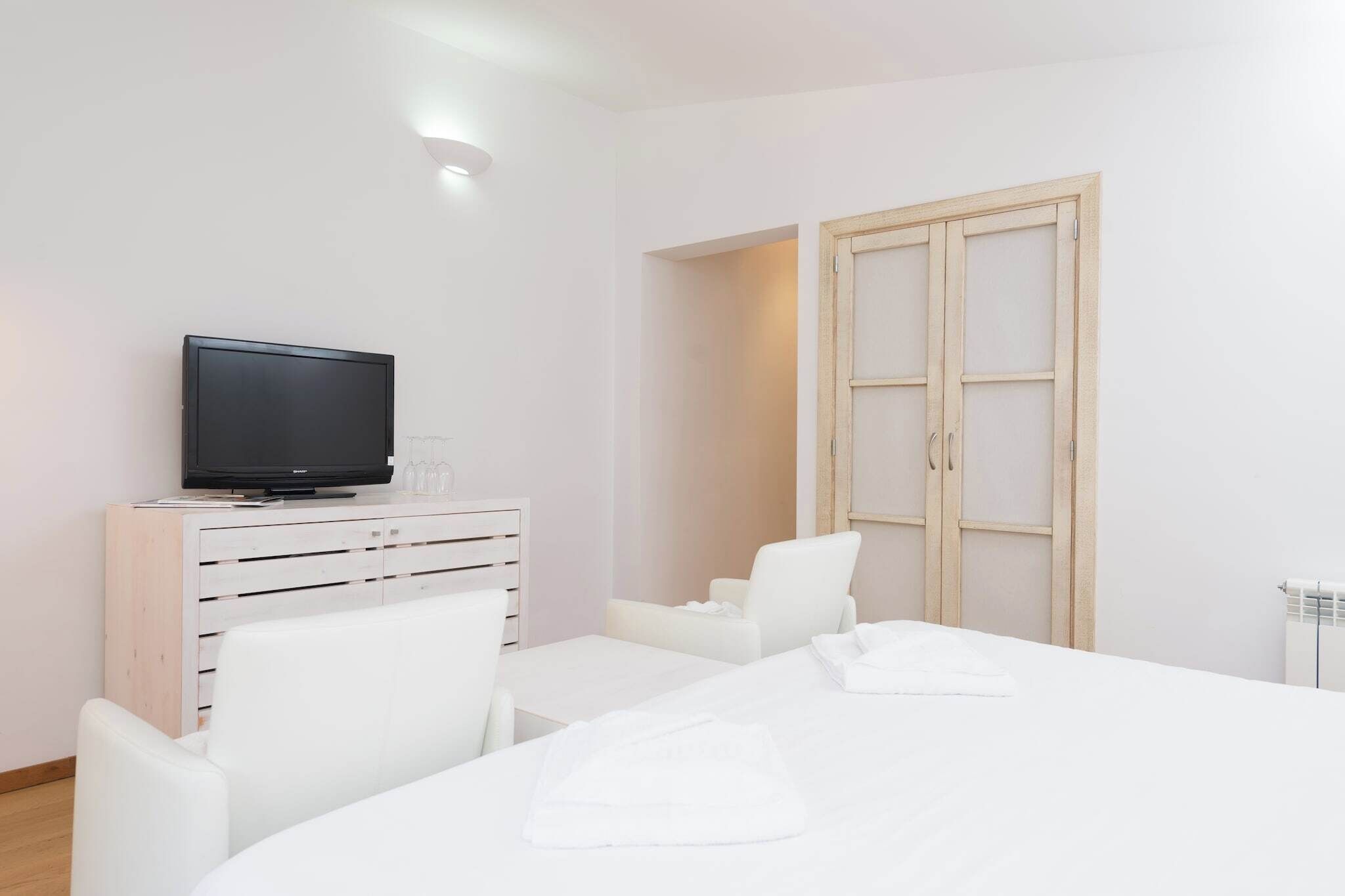 A hotel room with a bed, a television on a dresser, a white chair, and a wooden wardrobe.