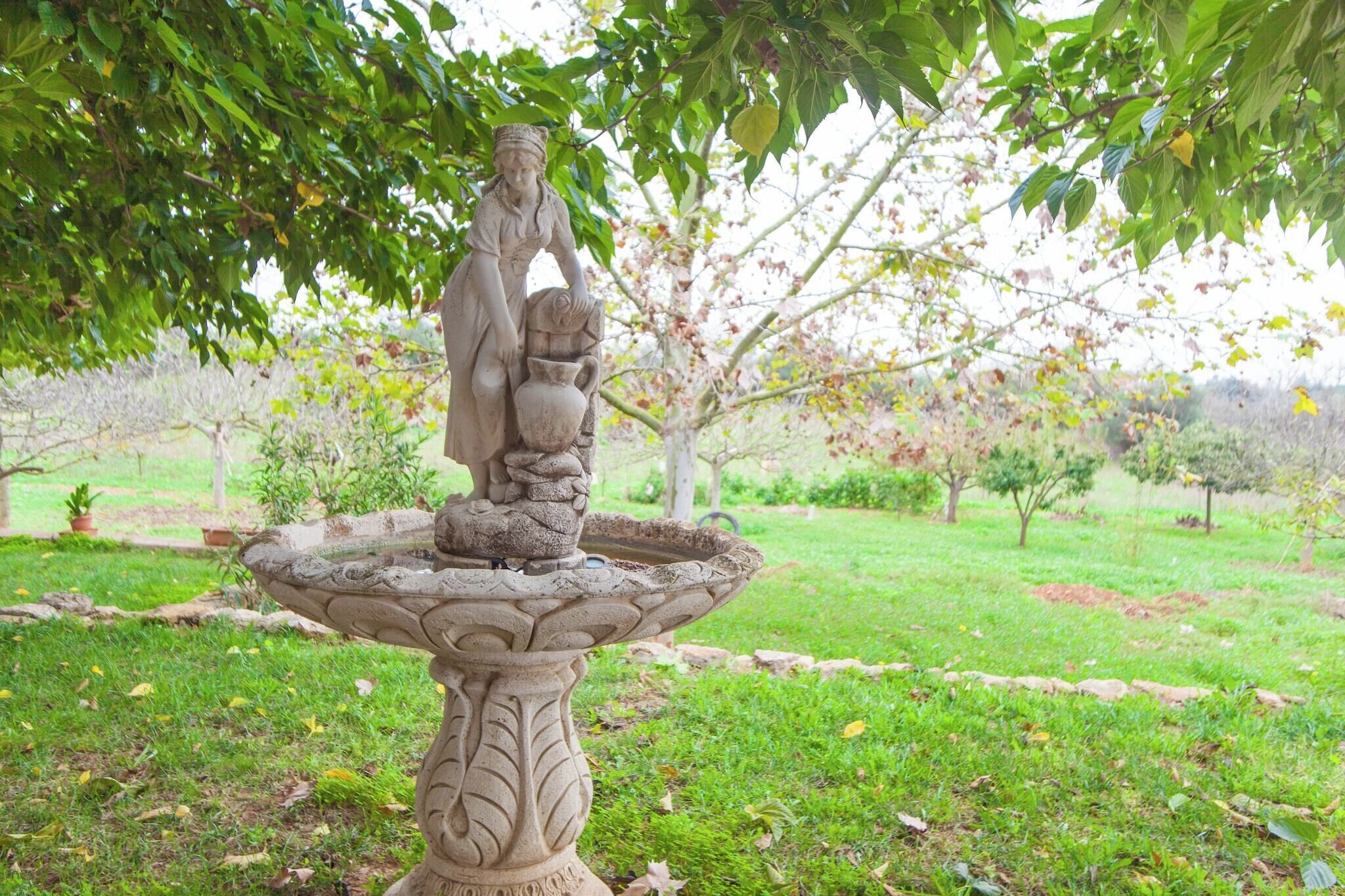 A garden statue with a fountain, surrounded by greenery and trees.