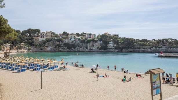 A beach with sun loungers and umbrellas, a lifeguard tower, and buildings in the background. - Sa Cova (cova De Rotana) - Villa With Private Pool (Manacor, Illes Balears)