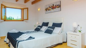 A bedroom with a large bed, a nightstand, a window with a view, and a painting on the wall. - Sa Cova (cova De Rotana) - Villa With Private Pool (Manacor, Illes Balears)