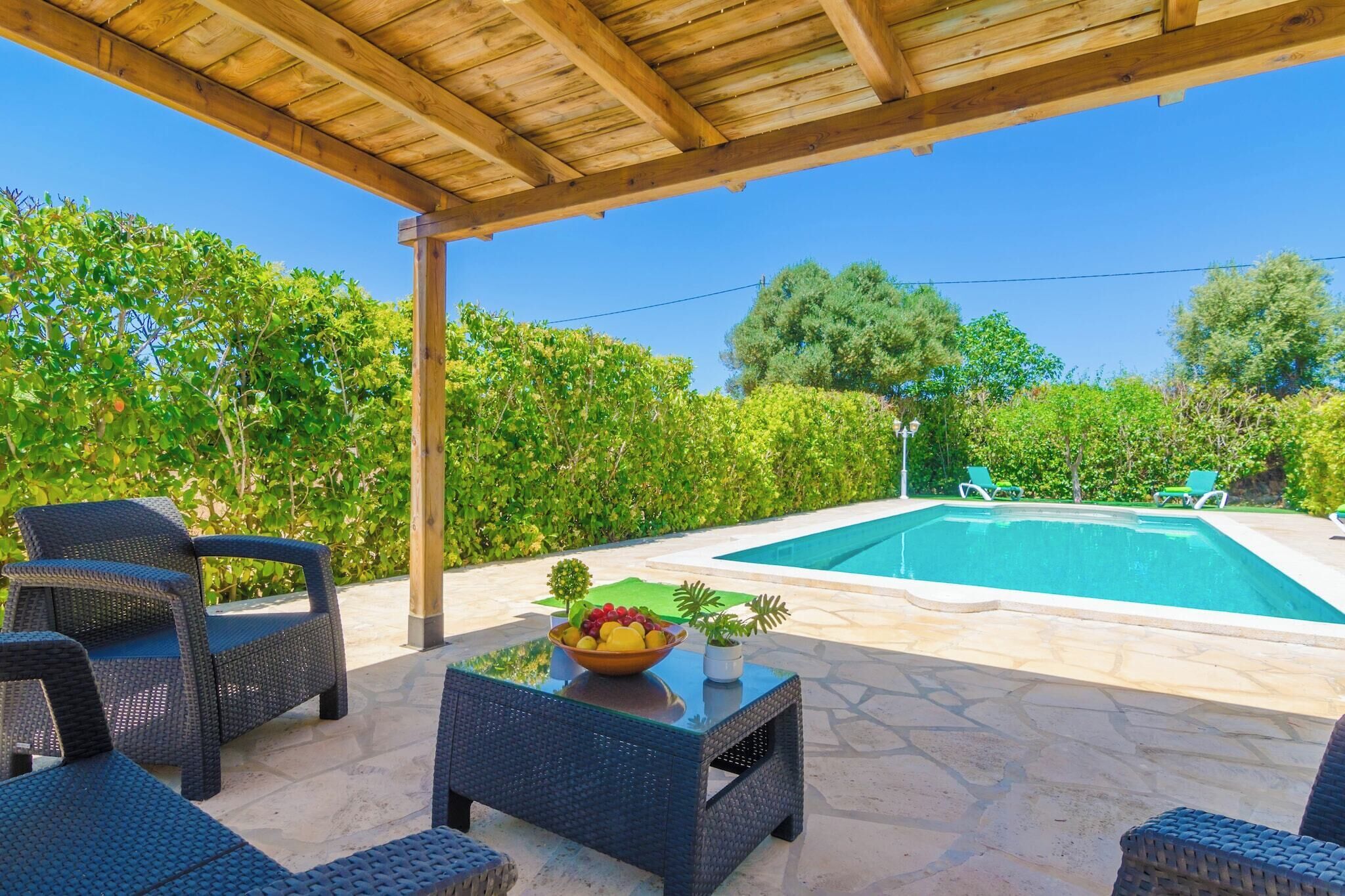 A covered outdoor area with a swimming pool, wicker furniture, and a bowl of fruit.