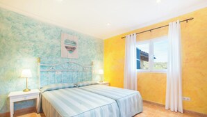 Une chambre à coucher avec un lit, deux tables de chevet avec des lampes, une fenêtre avec des rideaux et un mur orné d’un tableau.