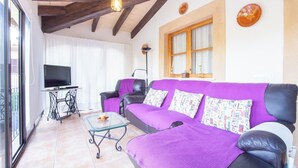 Un salon avec un canapé violet, un téléviseur posé sur une table et une fenêtre avec des rideaux.