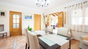 Un coin repas avec une table à plateau en verre, des chaises de couleur beige, un vase avec des fleurs et des portes en bois.