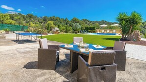 Un espace extérieur aménagé pour les repas, avec des meubles en osier et une vue sur une piscine et un jardin luxuriant.
