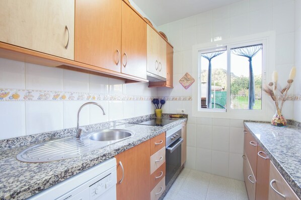 Cocina con encimeras de granito, armarios de madera, pileta de acero inoxidable y una ventana con cortinas.