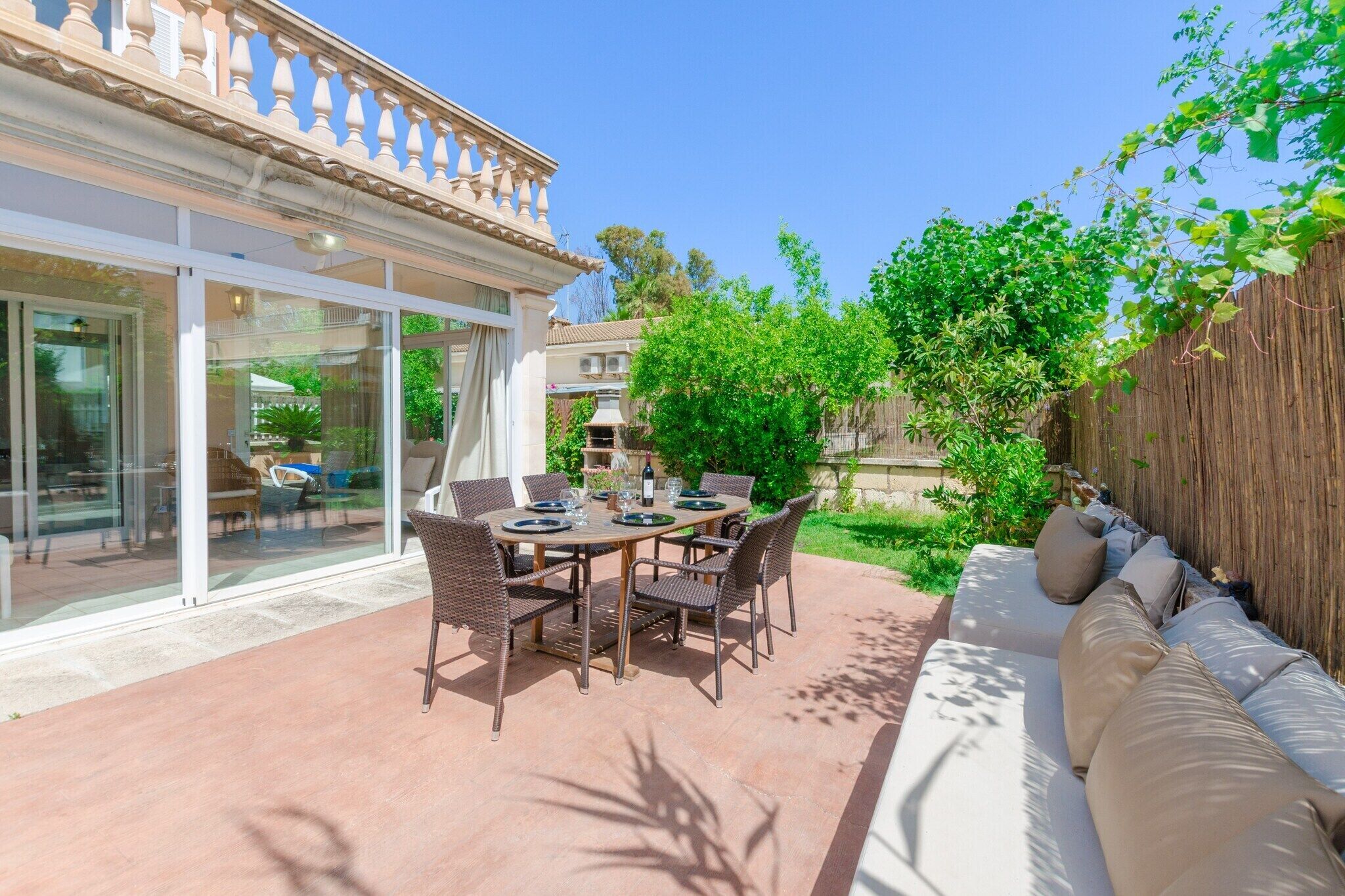 An outdoor patio with a round table set for dining, surrounded by wicker chairs.