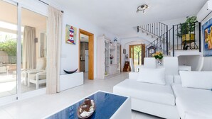 En rummelig opholdsstue med en hvid sofa, et sofabord i glas og en trappe til en etage over.
