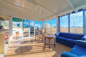 A sunlit patio with a blue sofa, wooden chairs, and a small table. - Europa 3b - Apartment In Port De Pollença (Port De Pollença, Illes Balears)
