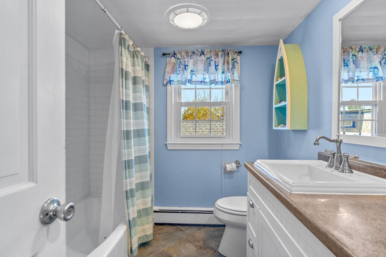 Une salle de bain équipée d’une douche, de toilettes, d’un lavabo et d’une fenêtre avec un rideau.