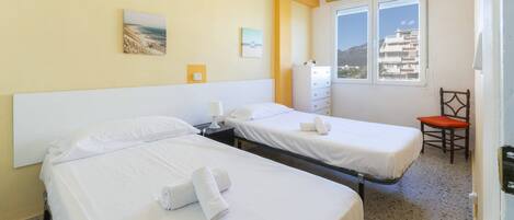 Ett hotellrum med två sängar, ett fönster med utsikt över byggnader, en stol och ett litet bord.