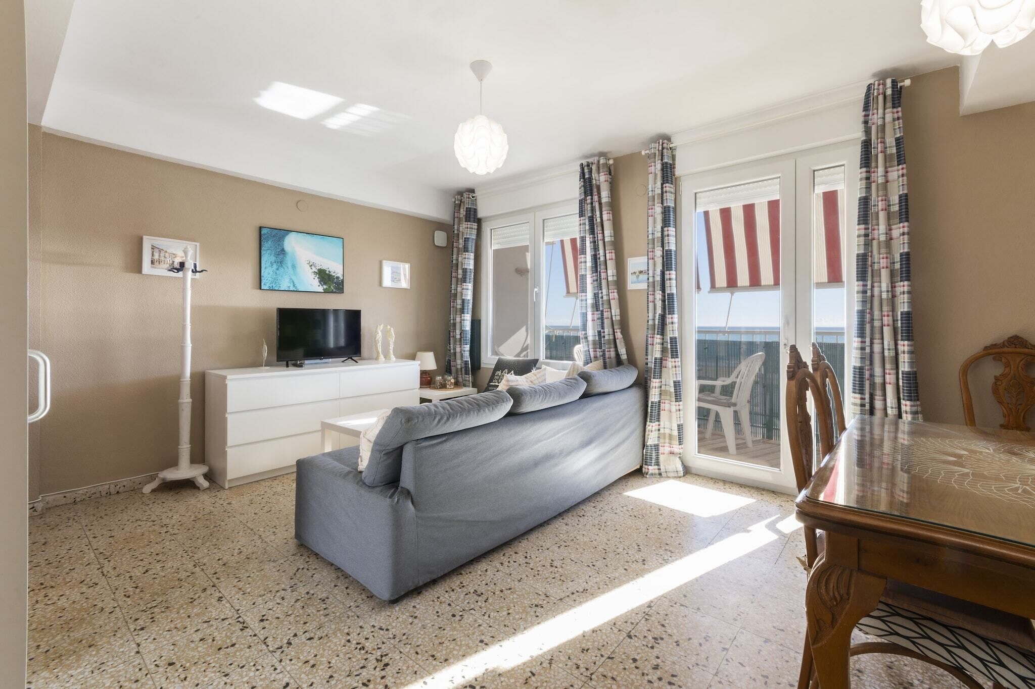 Una sala de estar con sofá, televisión, cómoda blanca, mesa de comedor y balcón con cortinas.