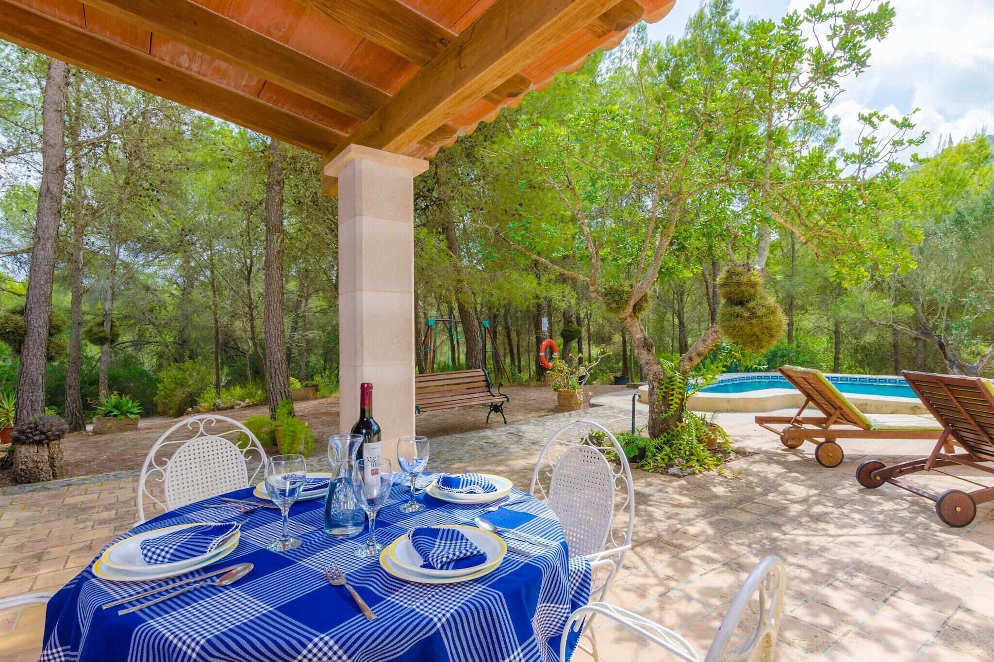 Un espace de restauration en plein air avec une table dressée pour deux personnes, entouré d’arbres et d’une piscine.