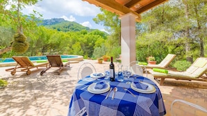 An outdoor dining area with a table set for two, surrounded by lounge chairs and a pool. - Casa Mas - Villa With Private Pool In Felanitx (Felanitx, Illes Balears)