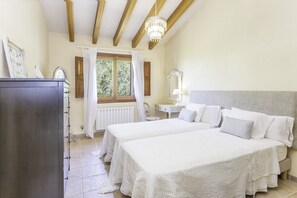 Un dormitorio con dos camas, un aparador, una ventana con cortinas y una araña.