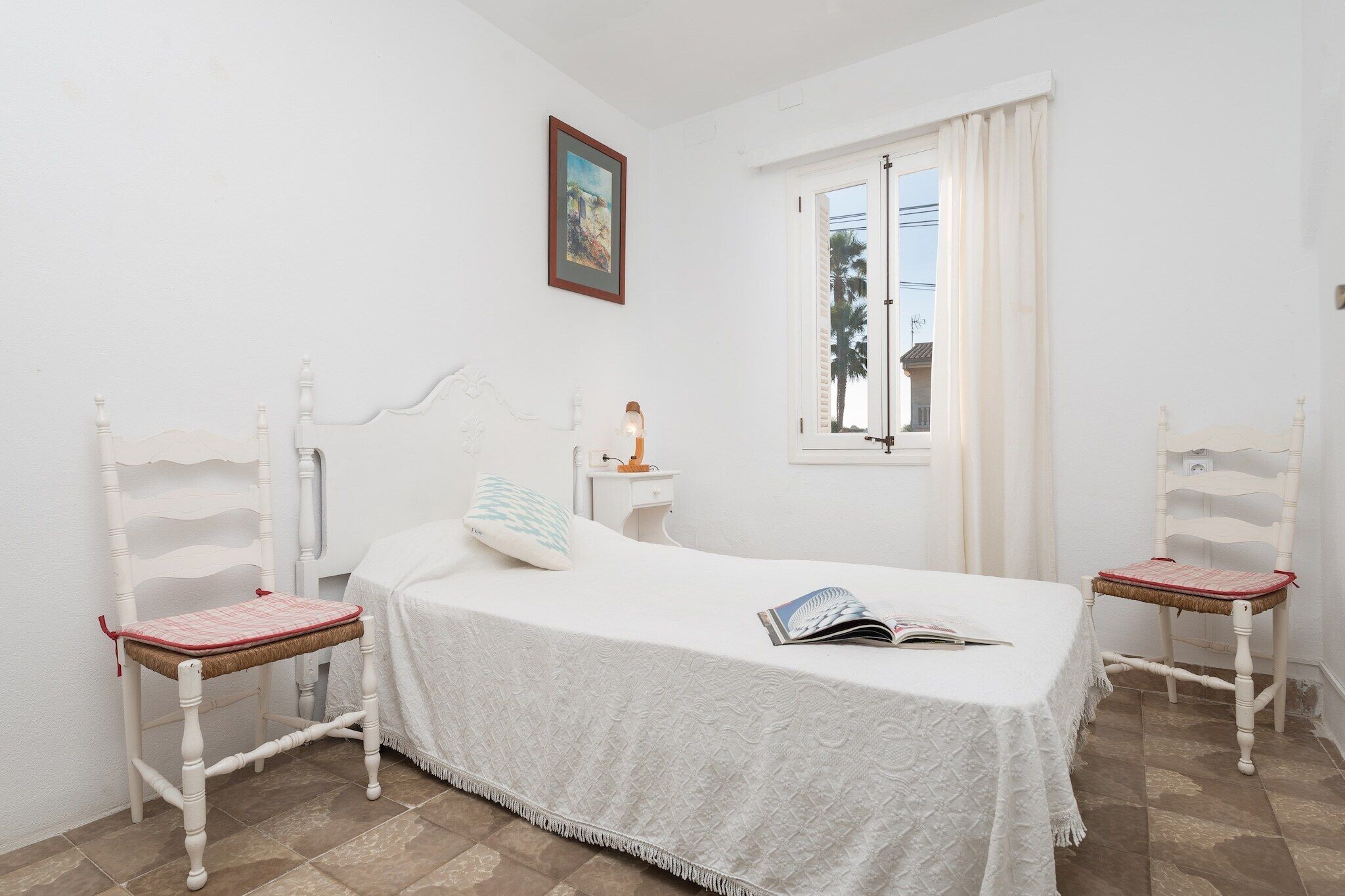A bedroom with a bed, two chairs, a window, and a painting on the wall.