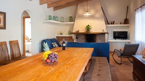 A wooden dining table with a fruit bowl, a wine bottle, and a television in the background. - Son Morro - Villa With Private Pool. Free Wifi (Santa Margalida, Illes Balears)