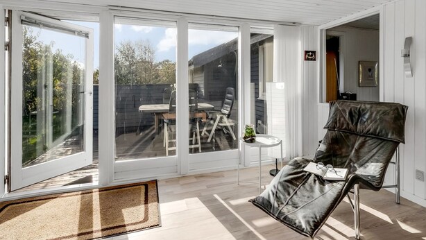 Habitación amplia con un gran ventanal corredero que da a un espacio exterior. Hay un sillón de cuero y una mesita con una planta.