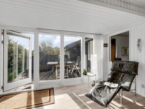 A spacious room with a large sliding glass door leading to an outdoor area. There is a leather chair and a small table with a plant. - "Pirjo" - 350m to the fjord by Interhome (Skjern)