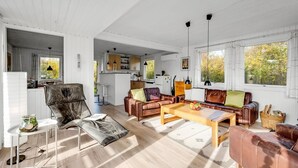 Un salón amplio con un conjunto de sofás, una mesa de centro y una mesa de comedor. Se ve una cocina al fondo con armarios y un refrigerador.