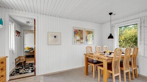 Un comedor con una mesa y sillas de madera, paredes blancas con paneles y obras de arte.