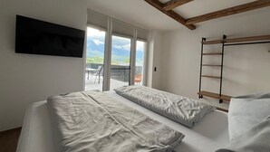 A bedroom with a bed, a TV, a window with a view of mountains, and a balcony. - Apartment in Saalfelden Near Ski Slopes (Saalfelden am Steinernen Meer)
