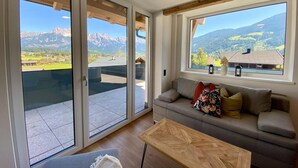 A modern living room with a sofa, a coffee table, and large windows offering mountain views. - Apartment in Saalfelden Near Ski Slopes (Saalfelden am Steinernen Meer)